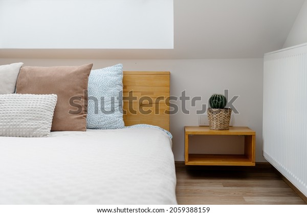 Part of cozy apartment with cactus houseplant on\
wooden side table near comfy bed with soft cushions in bright\
bedroom. Concept of weekend at\
home