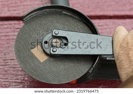 part of an electric powerful dangerous black with a cutting and grinding wheel and a protective shield of a grinder and a key to remove the circle on a brown wooden table on the street during the day