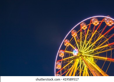 Part of ferris wheel against a blue sky background with lights neby night lighting