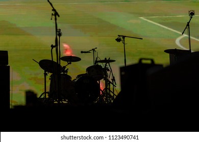 Part Of Football Soccer Game With Players In Red And White And Soccer Net On Goal Showing On A Big Screen Before The Beginning Of The Music Concert, With A Black Silhouette Of A Drum Set In Front