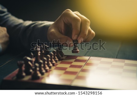 part of human hand moves chess figure on chess board in retro color tone and artificial light