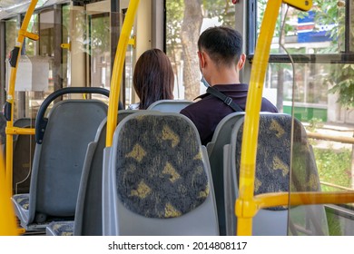 Part of the interior of a modern bus, in the foreground you can see empty seats, yellow handrails and two seated passengers, a man and a woman, a view from the back.