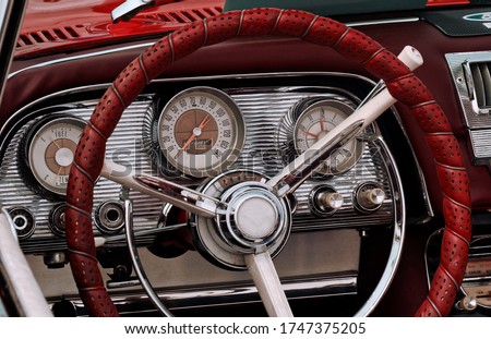 Part of the interior of an oldtimer sports luxury car with steering wheel, speedometer, fuel, clock dials, gear lever, front panel.