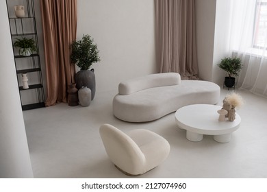 Part of large cozy and light living-room with white round table with handmade vases, comfortable sofa and armchair in apartment