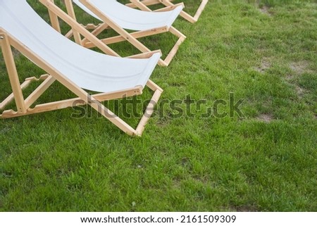 Part of a lightweight folding chair for outdoor recreation. An empty white wooden chaise longue on the green grass of a fresh lawn with a place to copy. High quality photo