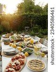 Part of long table served with various food and snacks prepared for outdoor family dinner standing in front of camera in the garden
