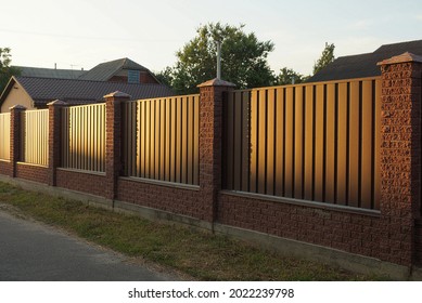 part of a long wall of a fence made of brown bricks and metal outside in the evening