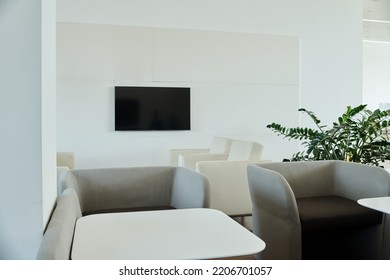 Part of modern comfortable openspace office with tv screen on wall, white leather and grey velvet armchairs and small square tables