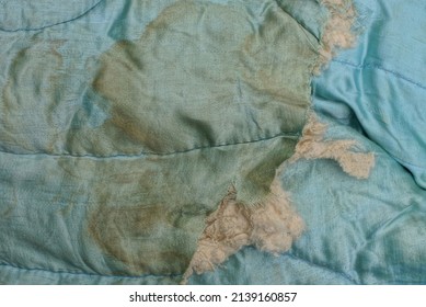 Part Of An Old Blanket Made Of Dirty Brown Blue Cloth With A Torn Hole And Gray Cotton Wool