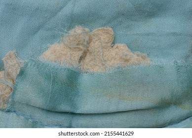 Part Of An Old Blanket Made Of Dirty Blue Cloth With A Torn Hole And Gray Cotton Wool