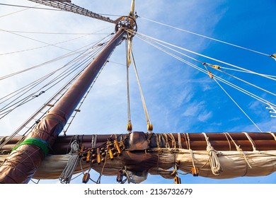 Part Of An Old, Wooden Sailing Ship With A Mast, Folded Sail And Stretched Sail Ropes.