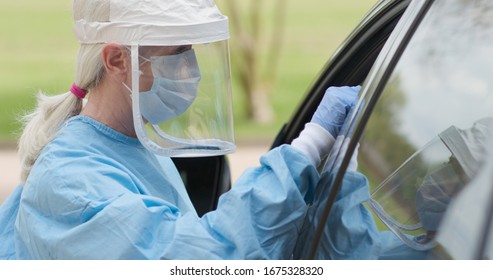 As part of the operations of a coronavirus mobile testing unit a healthcare worker dressed in full protective gear swabs an unseen person sitting inside of a vehicle.