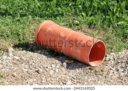 Part of orange PVC large diameter construction pipe covered with yellow polyurethane foam or PU foam left on side of local construction site gravel path next to uncut grass on warm sunny spring day