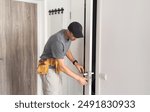 As part of process of installing interior doors in new house, a trim worker uses hammer to strike the door jambs