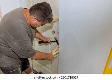 As part of process of installing interior doors in new house, a trim worker uses hammer to strike the door jambs