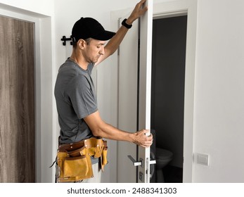 As part of process of installing interior doors in new house, a trim worker uses hammer to strike the door jambs