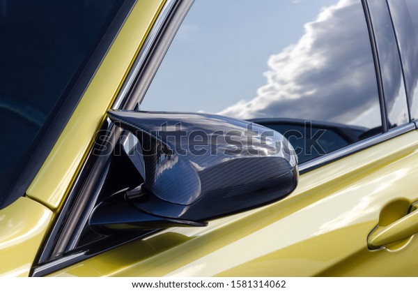 part of a sports\
expensive car. carbon mirror. golden color car. on the door window\
the reflection of the sky