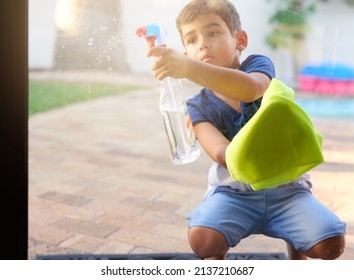 Part of the spring cleaning team. Shot of a little boy washing a glass door at home.