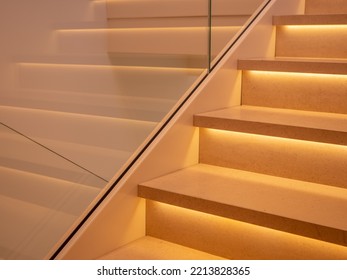 part of stairs in light marble with bright leds below the steps, wall with a glass plate