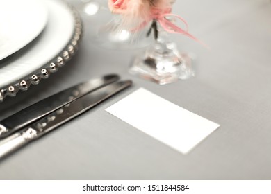 Part of stylish table setting with plate and cutlery. Nearby lies a white business card. Copy space.
