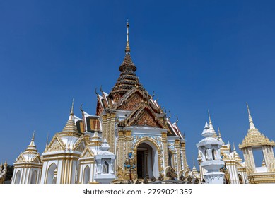 Part of the temple complex of Wat Klang Bang Kaew in Nakho Pathom, just outside of Bankgkok, Thailand. White buildlings intricately decorated sit under a deep blue sky.
