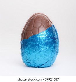 Part Unwrapped Blue Foil Covered Chocolate Easter Egg Isolated Against White Background