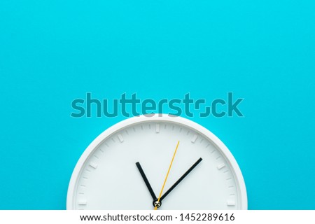 Part of white wall clock with yellow second hand hanging on wall. Close up image of plastic wall clock over turquiose blue background with copy space.