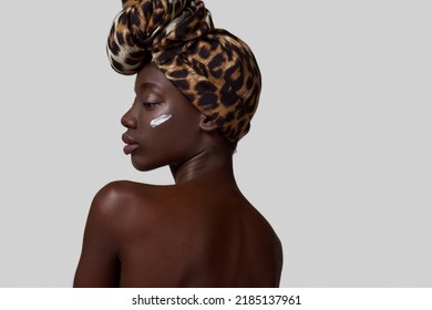 Partial Back Of Stylish Black Girl With Cosmetic Cream On Her Face. Attractive Young Slim Woman Wearing Traditional African Turban. Body And Skin Care. White Background. Studio Shoot. Copy Space