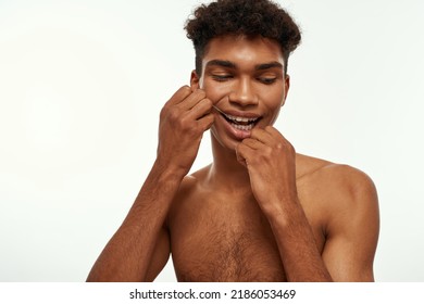 Partial Of Black Guy Brushing His Teeth With Dental Floss. Young Brunette Curly Man With Naked Torso. Dental Care And Hygiene. Isolated On White Background. Studio Shoot. Copy Space