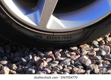 Partial close up image of a low profile tire on gravel surface with size markings and country of origin visible and the tire is attached to slightly worn aluminium rim