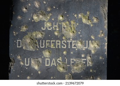 A Partial Damaged Bible Inscription In German On A Tombstone Which Is Littered With Bullet Holes From War. Translation 