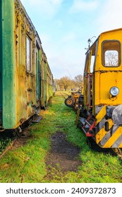 Partial and front view of old yellow ruined train control cabin and corroded metal passenger carriage, disused tracks at old station, cloudy autumn day in As, Limburg, Belgium