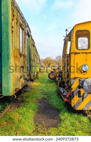 Partial and front view of old yellow ruined train control cabin and corroded metal passenger carriage, disused tracks at old station, cloudy autumn day in As, Limburg, Belgium