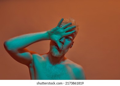 Partial Image Of Albino Caucasian Guy Covering His Half Face And Looking At Camera. Young Bearded Blonde Man Of Generation Z With Naked Torso. Isolated On Orange Background. Studio Shoot. Copy Space