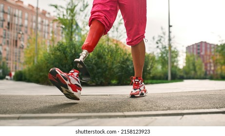 Partial Image Of Athletic Girl With Artificial Leg Has Disability Walking On Pavement Road On City Square. Young Woman Wear Sportswear. Concept Of Healthy Lifestyle. Conquering Adversity And Willpower