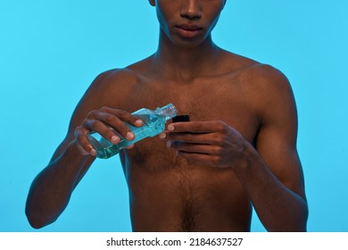 Partial Image Of Black Guy Pouring Shower Gel In Bottle Cap. Obscure Face Of Young Man With Naked Torso. Hygiene And Body Care. Isolated On Light Blue Background. Studio Shoot. Copy Space