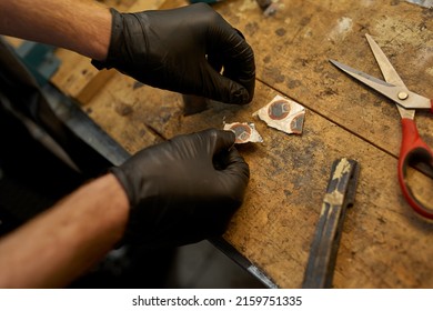 Partial Image Of Cycling Mechanic Hands In Gloves Holding Bicycle Patch Over Table For Glueing On Bike Tube In Workshop. Bike Service, Repair And Upgrade. Wooden Desk With Glue And Scissors