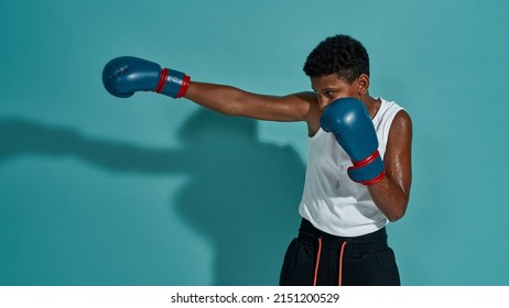 Partial image of focused black boy boxer boxing. Male child wearing sportswear and boxing gloves. Modern healthy and sports lifestyle. Isolated on turquoise background. Studio shoot. Copy space