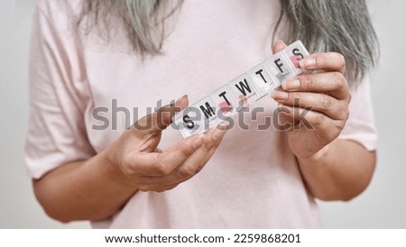 Partial image of mature woman holding plastic package with pills on all week days. Health care and treatment. Concept of modern elderly lifestyle. Isolated on white background. Studio shoot