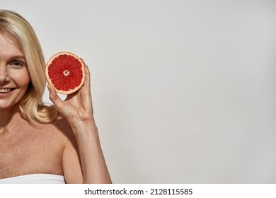 Partial Image Of Middle Aged Caucasian Woman Holding Sliced Ripe Organic Grapefruit. Obscure Face Of Smiling Blonde Female Looking At Camera. Beauty Concept. White Background In Studio. Copy Space