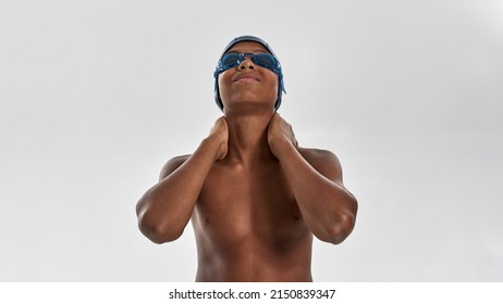 Partial Image Of Smiling Black Boy Swimmer Touch His Neck And Look At Camera. Male Youngster Wear Swimming Cap And Goggles. Modern Child Sportive Lifestyle. White Background. Studio Shoot. Copy Space