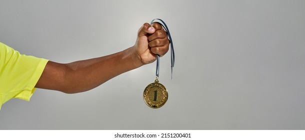 Partial Image Of Successful Athletic Black Boy Hand Hold Champion Gold Medal. Concept Of Modern Youngster Sportive Lifestyle. Victory And Triumph. Isolated On Grey Background. Studio Shoot. Copy Space