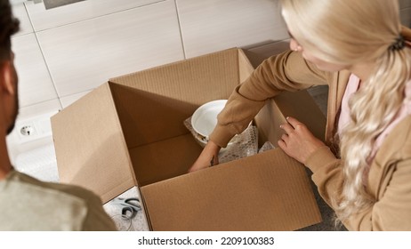 Partial Image Of Young Couple Packing Cooking Utensils In Air Bubble Film In Cardboard Box At Kitchen. Blonde Girl With Tattoo And Man Moving To New Apartment. Concept Of Home Relocation