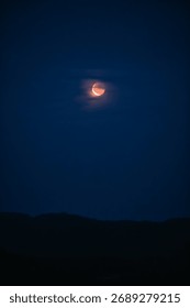Partial lunar eclipse with red moon emerging through clouds in the dark night