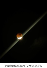 Partial lunar eclipse showing deep red blood moon with bright lower edge, dramatic diagonal light streak crossing the black night sky.