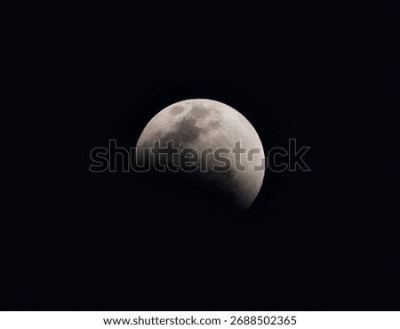 Partial lunar eclipse showing Earth's shadow crossing the moon's surface with visible crater details and maria against black night sky, capturing celestial event and astronomical phenomenon