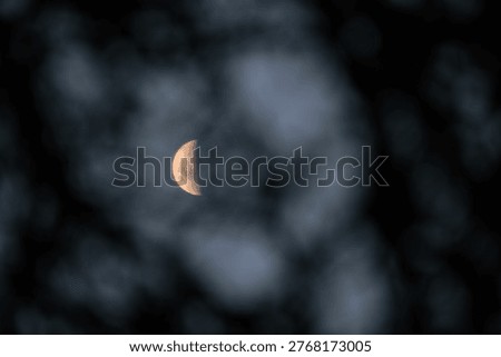 Partial lunar eclipse viewed through soft night clouds, featuring a glowing orange crescent moon with a moody, atmospheric feel
