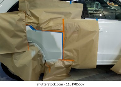 Partial Painting Of The Rear Right Door Of The White Car In The Body Repair Shop. The SUV Is Covered With Pieces Of Yellow Thick Paper, Pasted With A Blue And Orange Tape.