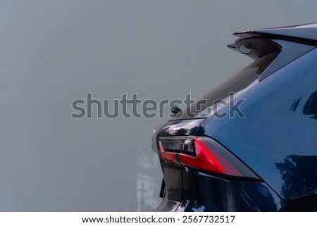Partial rear view of a dark blue black SUV. Possibly based on the taillight design. The car is parked against a plain light-colored background.