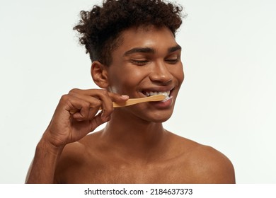 Partial Of Smiling Black Guy Brushing His Teeth With Toothpaste. Young Brunette Curly Man With Naked Torso. Dental Care And Hygiene. Isolated On White Background. Studio Shoot. Copy Space